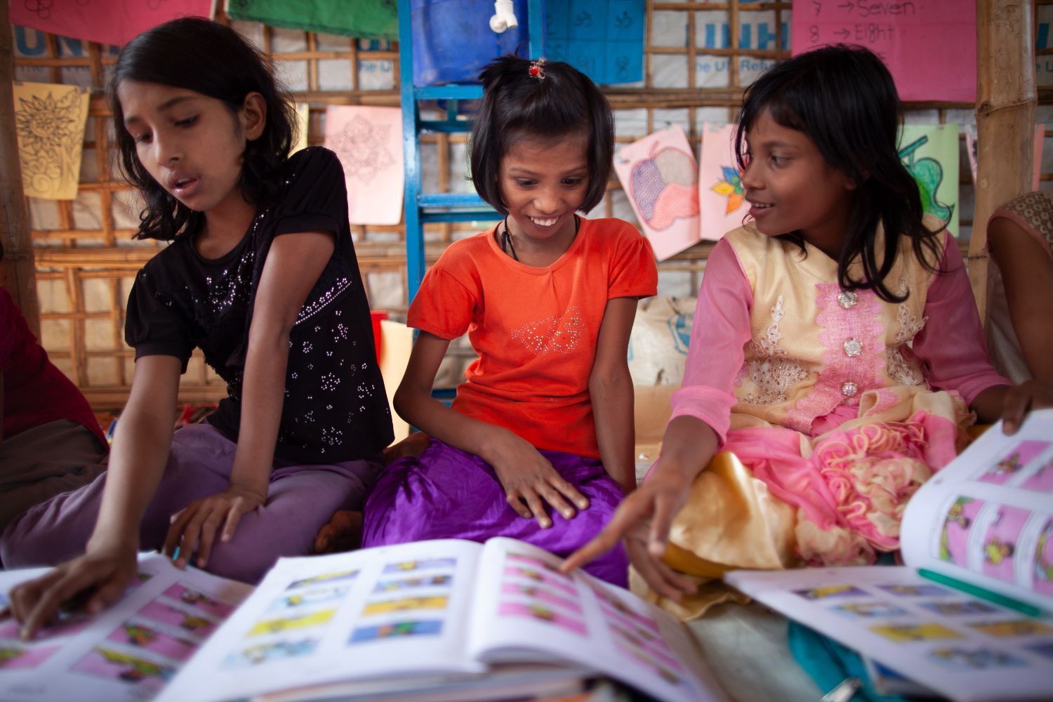 A group of three girls read from learning materials in a learning center supported by Education Cannot Wait