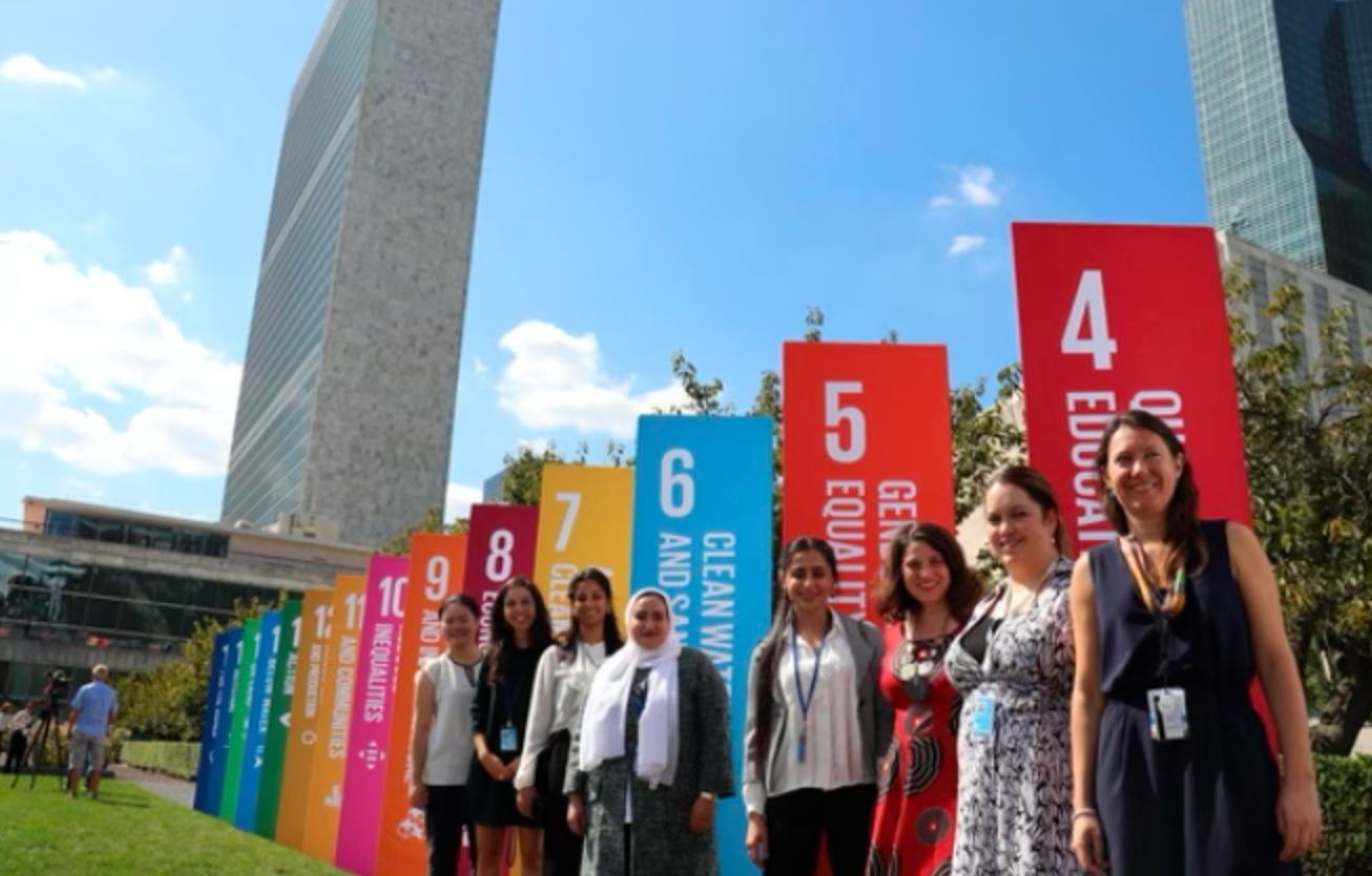 Advocates stand in front of SDG Action signs at the UN HQ.